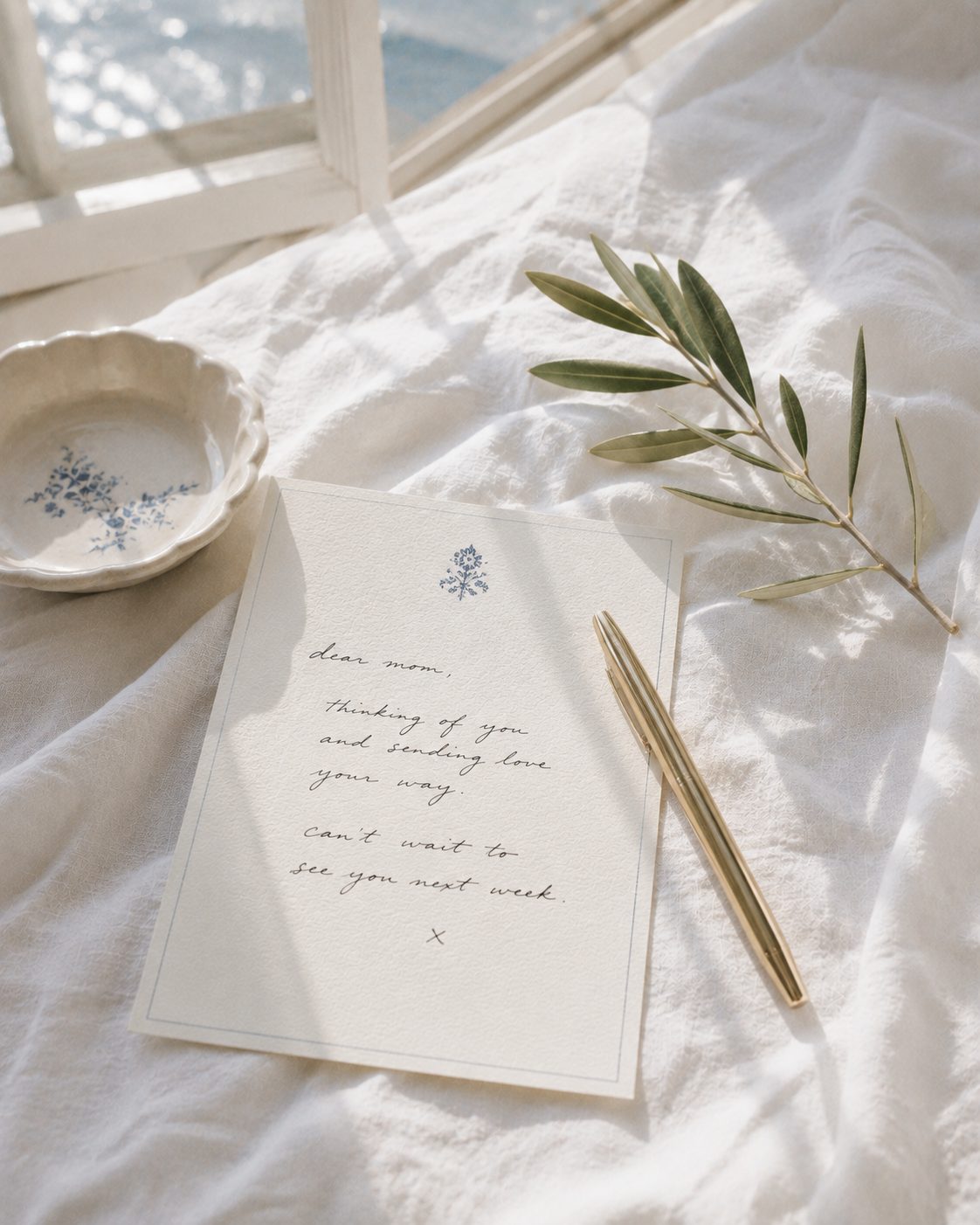 A handwritten note on cream stationery with an olive sprig and a gold pen on white linen